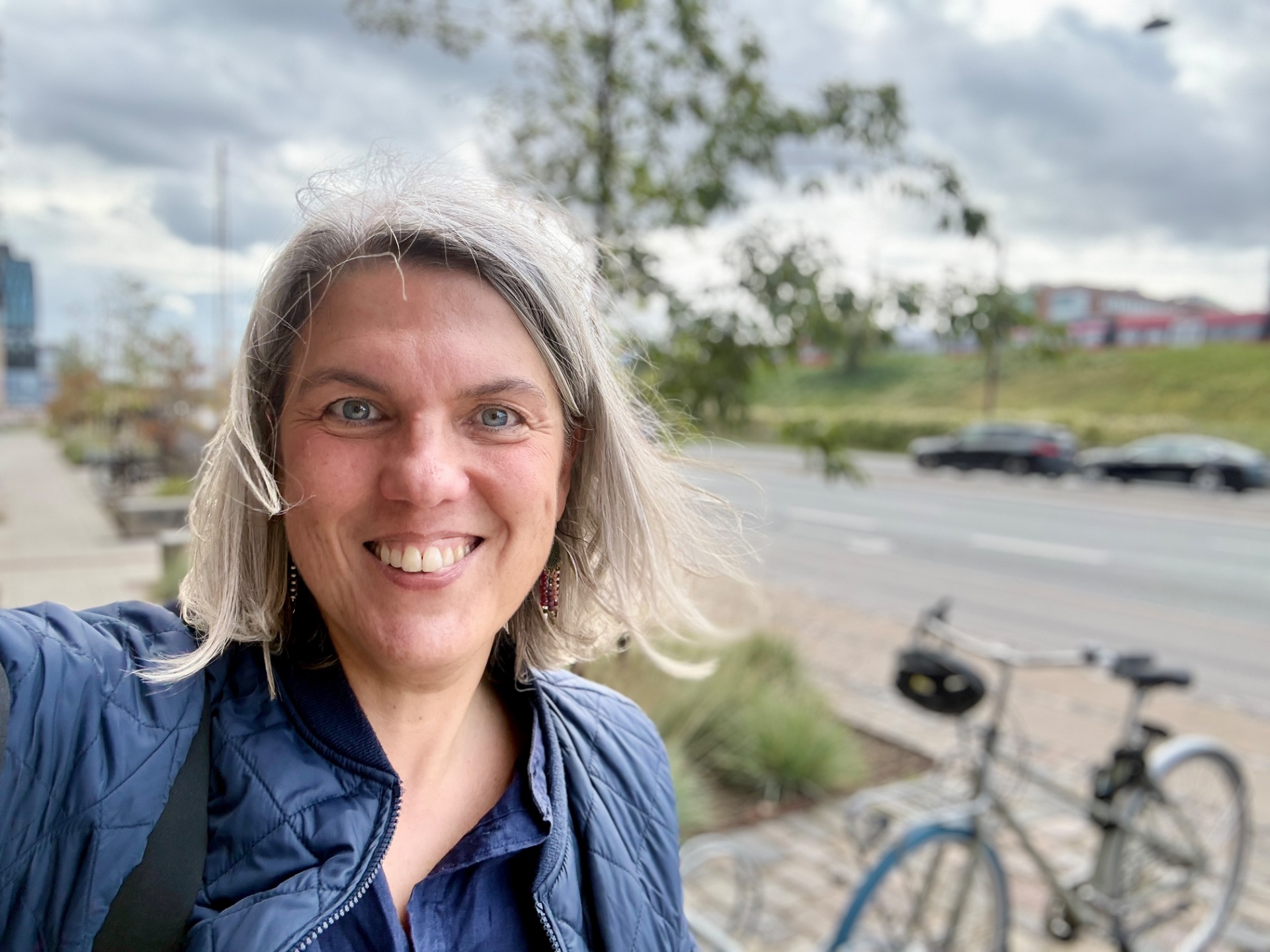 Rebecca Wessel Knaack smiler på en gade en grå dag, med en cykel i baggrunden.